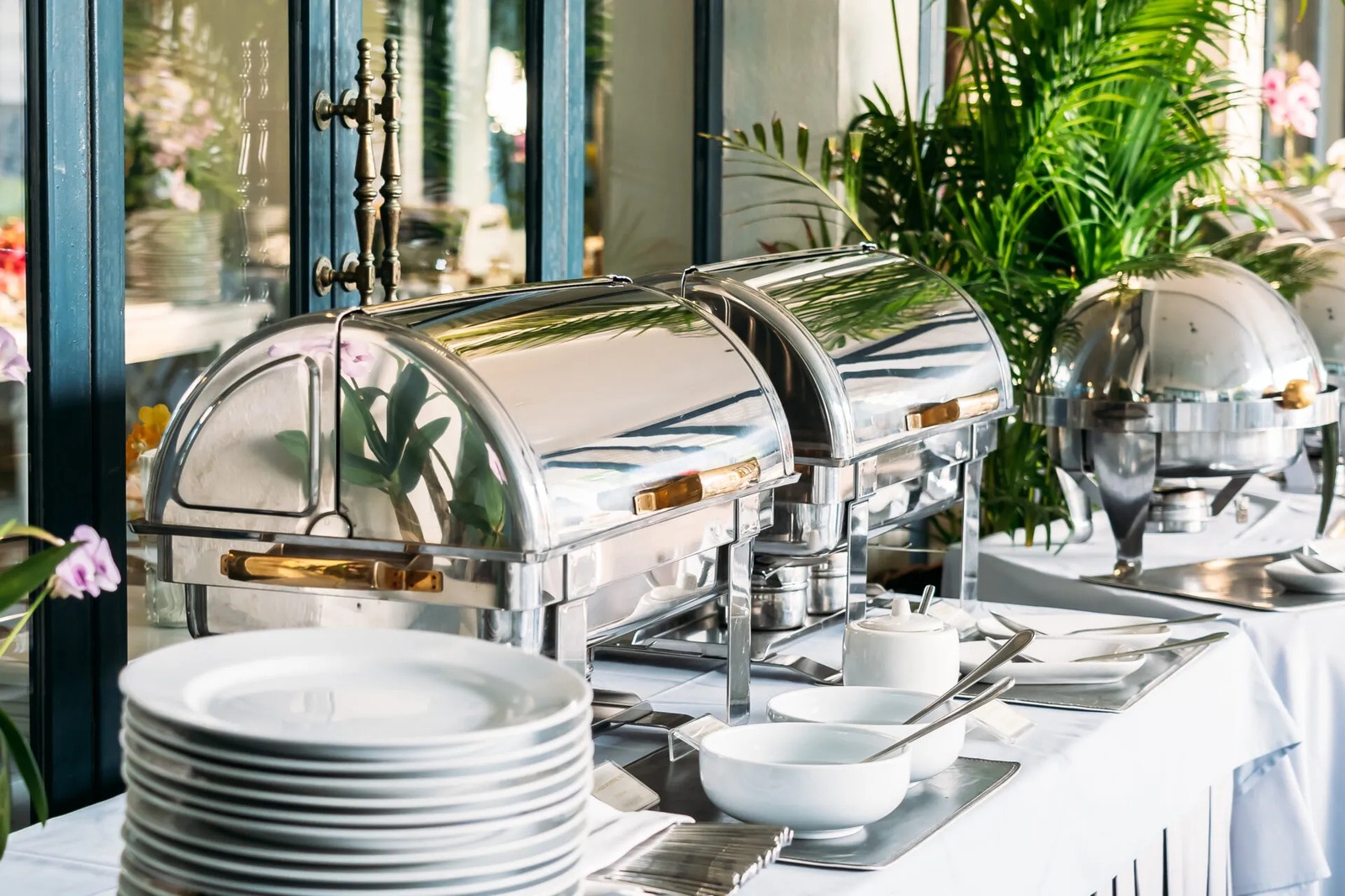 Buffet with silver chafing dishes and stacks of white plates