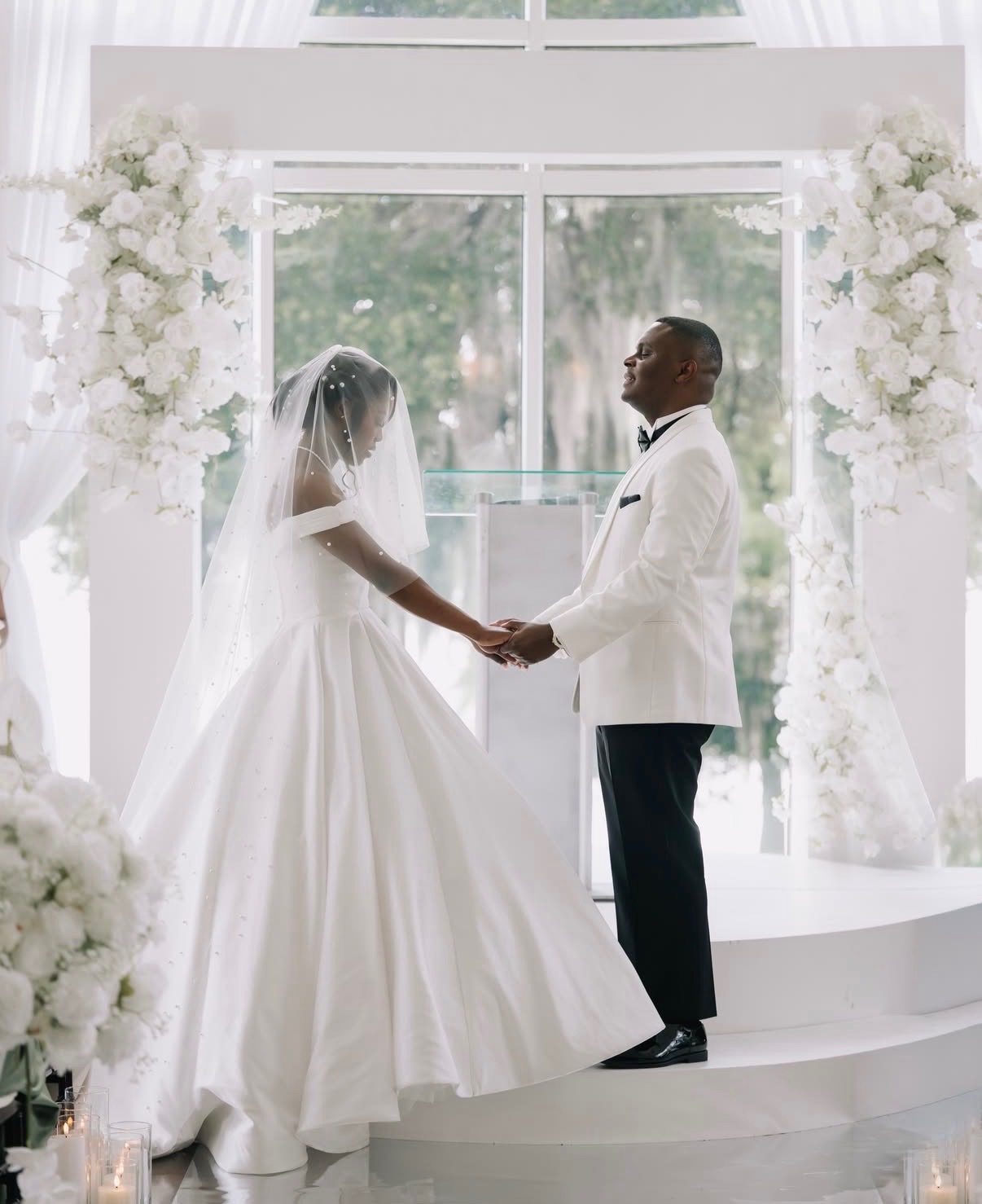 Bride and groom holding hands at the altar between white floral columns