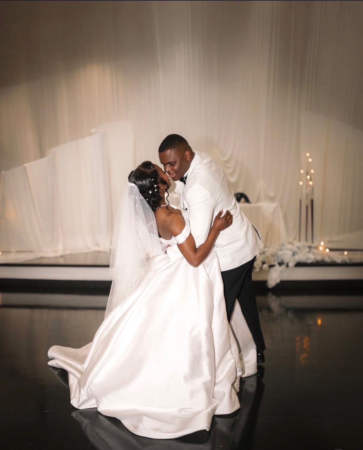 Bride and groom sharing their first dance in front of ivory draping and candlelight