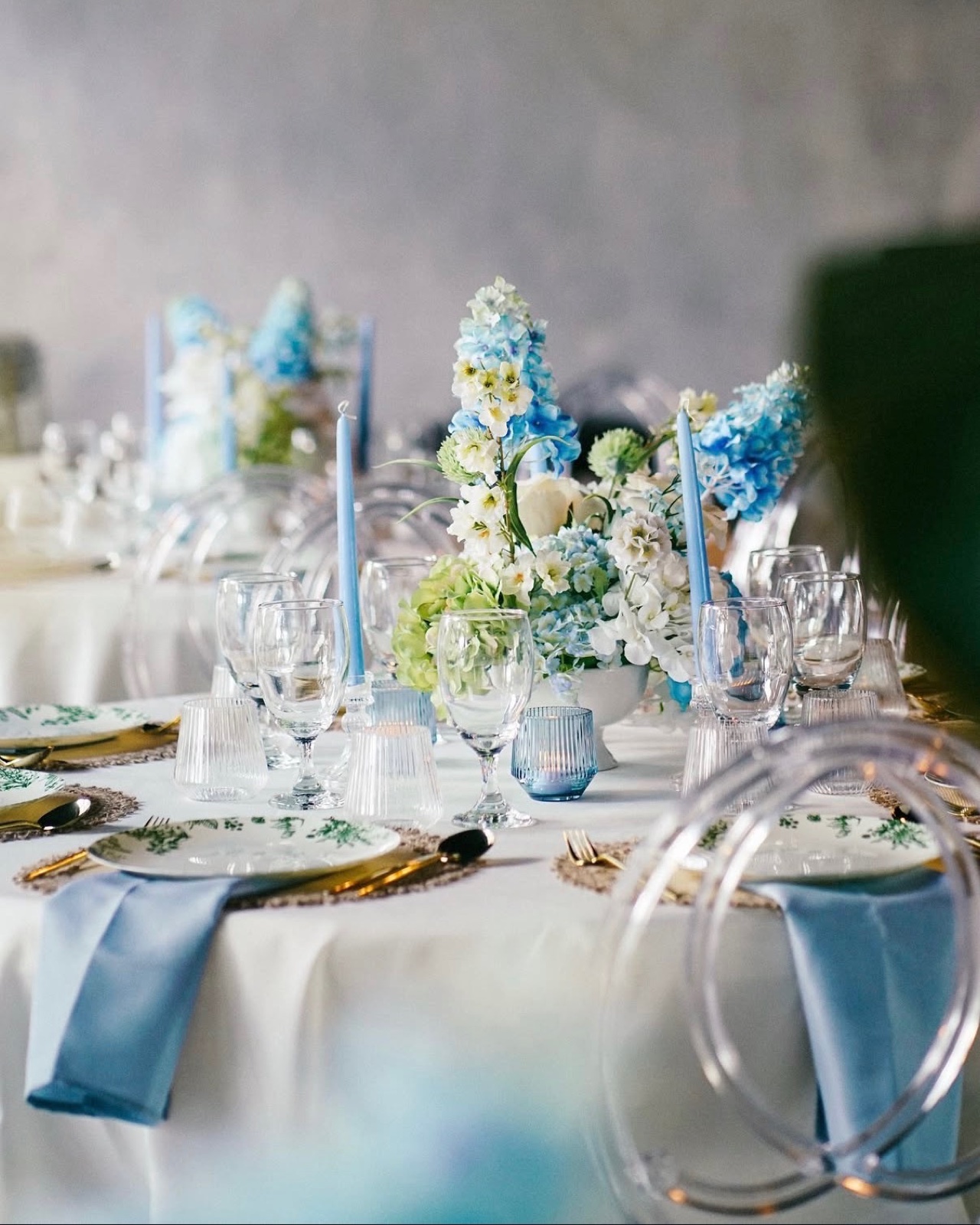 Round table with blue hydrangeas and delphinium, pale blue taper candles, botanical plates and gold flatware