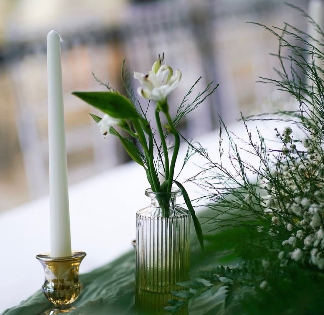 White taper candle and a single bloom in a ribbed glass bud vase on a sage runner