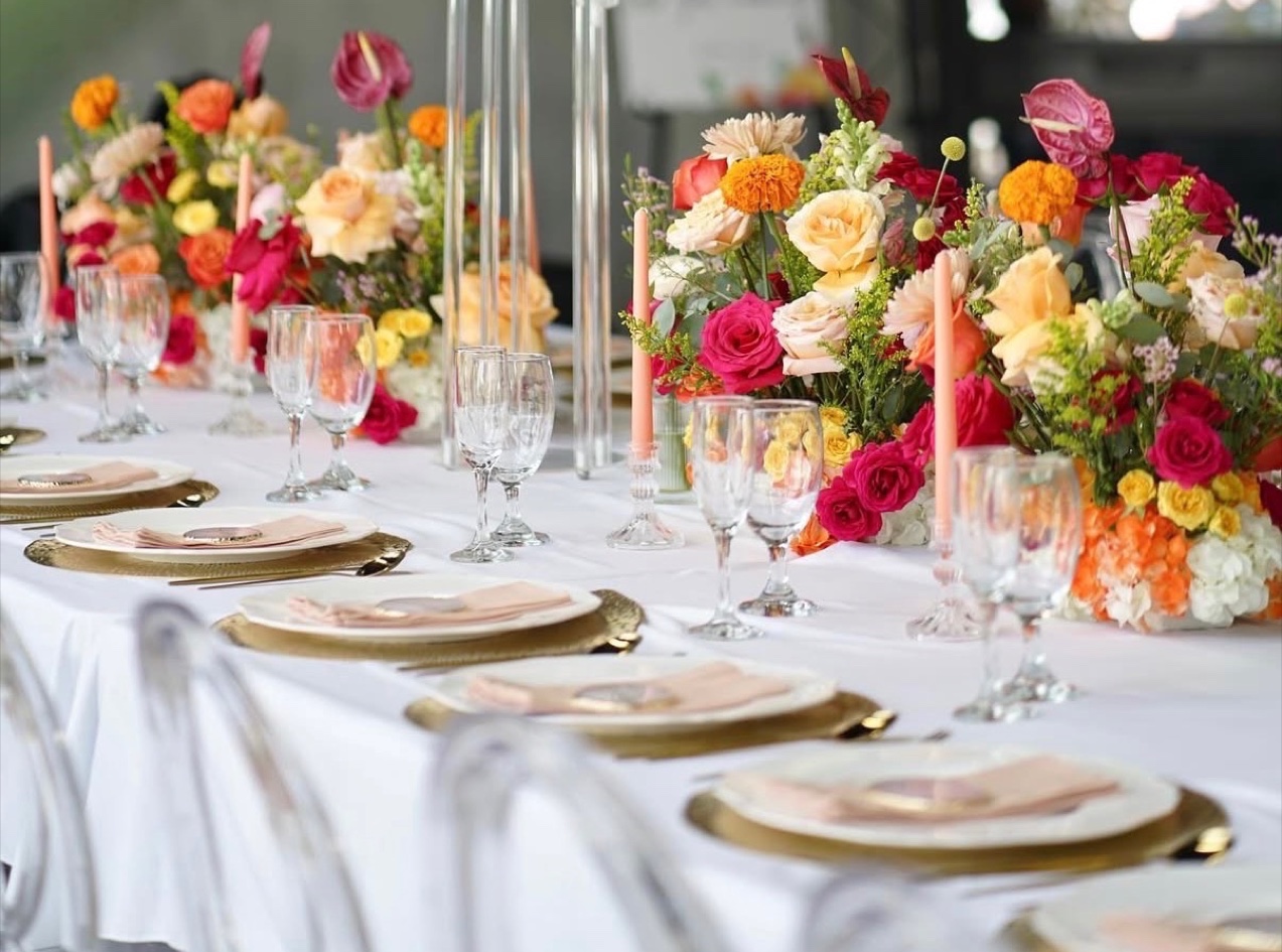 Long table with bright roses, marigolds and anthuriums, crystal candelabras and gold chargers