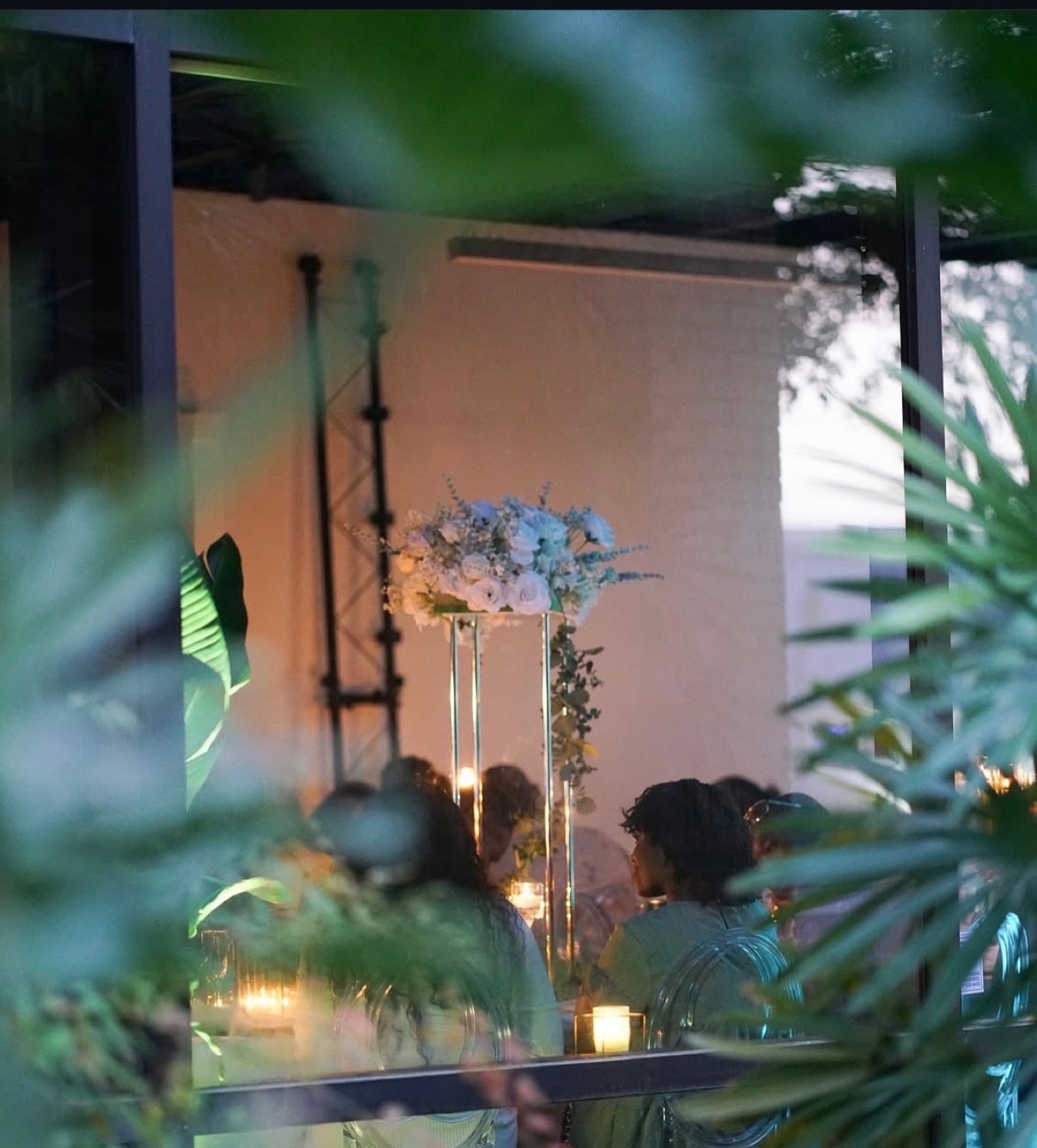 Guests dining by candlelight under tall white floral arrangements