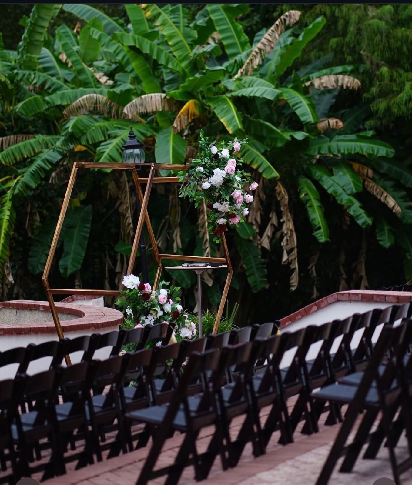 Wooden hexagon arch with pink and white roses in a tropical garden, rows of black chairs