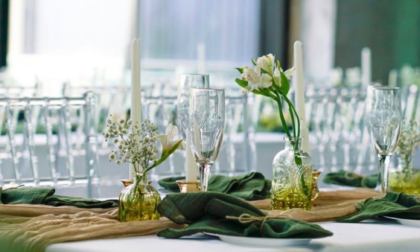 Table set with forest green napkins, bud vases, taper candles and champagne flutes